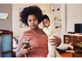 A woman holding a baby in one arm and texting on a phone in her other hand